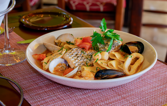 Filete de robalo salteado con camarón, callo de almeja, aros de calamar, almejas chirla, mejillones negros, vino blanco y bisque de langosta. Servido con pasta paccheri.